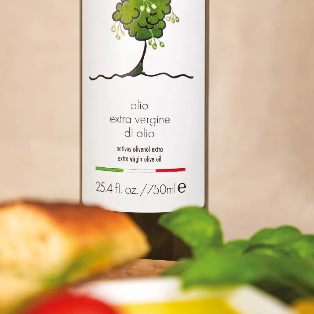 750 ml Flasche Olio extra vergine di oliva mit Olivenbaum-Logo, davor Brot und Basilikum.