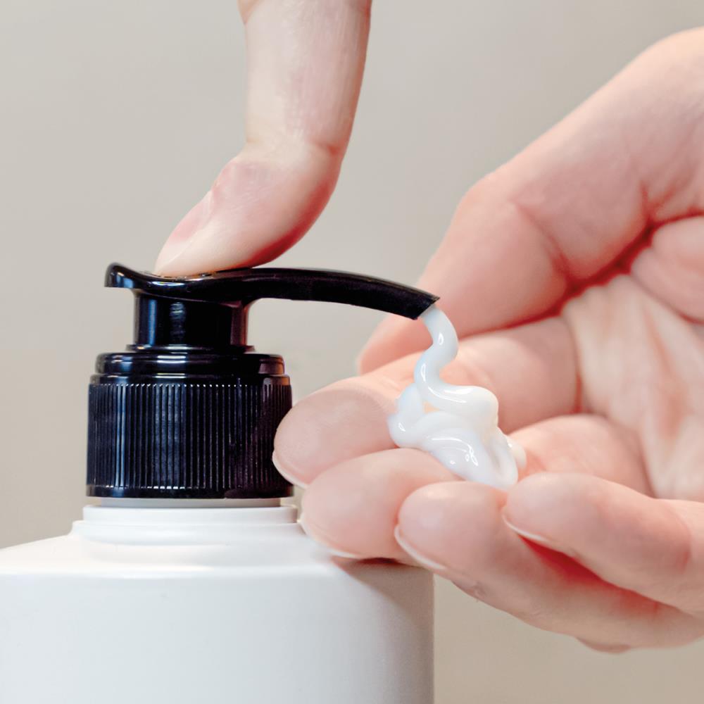 Hand drückt weißen Leave-in Conditioner aus einer Flasche mit Pumpkopf