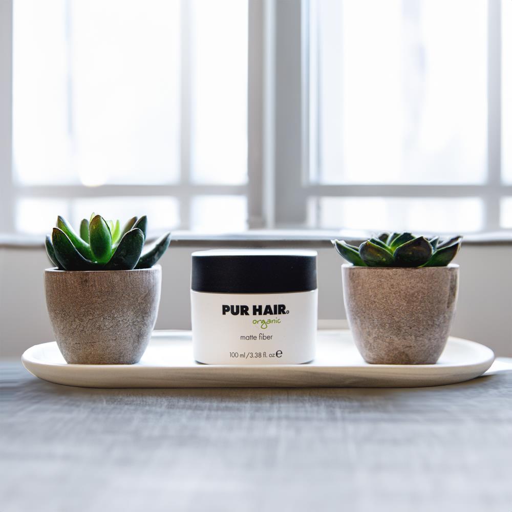 PUR HAIR Organic Matte Fiber 100 ml Dose, auf einem Tablett zwischen zwei kleinen Sukkulenten vor einem Fenster arrangiert