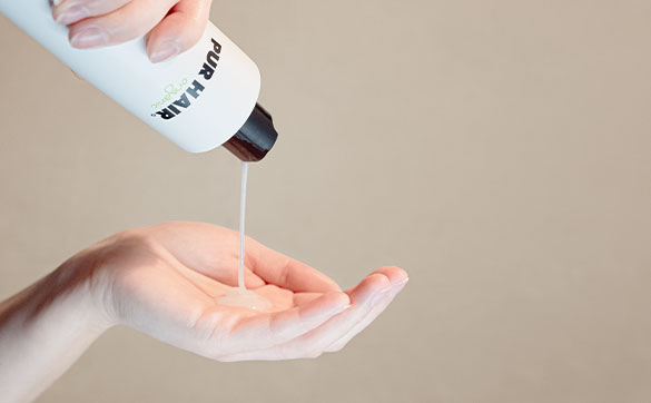 Hand hält PUR HAIR Organic Flasche, aus der Shampoo in eine geöffnete Handfläche gegossen wird