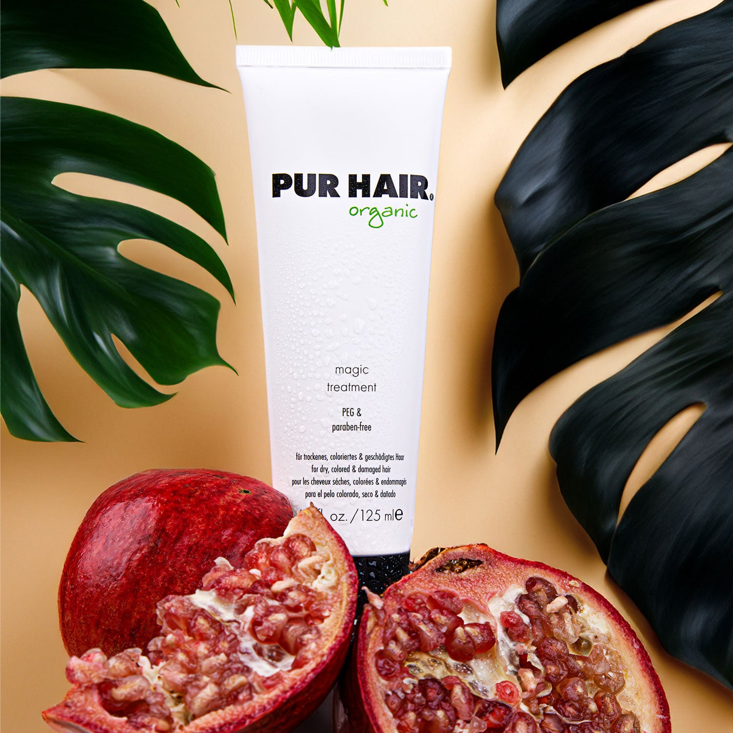 PUR HAIR Organic Magic Treatment in weißer Tube (125 ml) vor tropischen Blättern und aufgeschnittenem Granatapfel