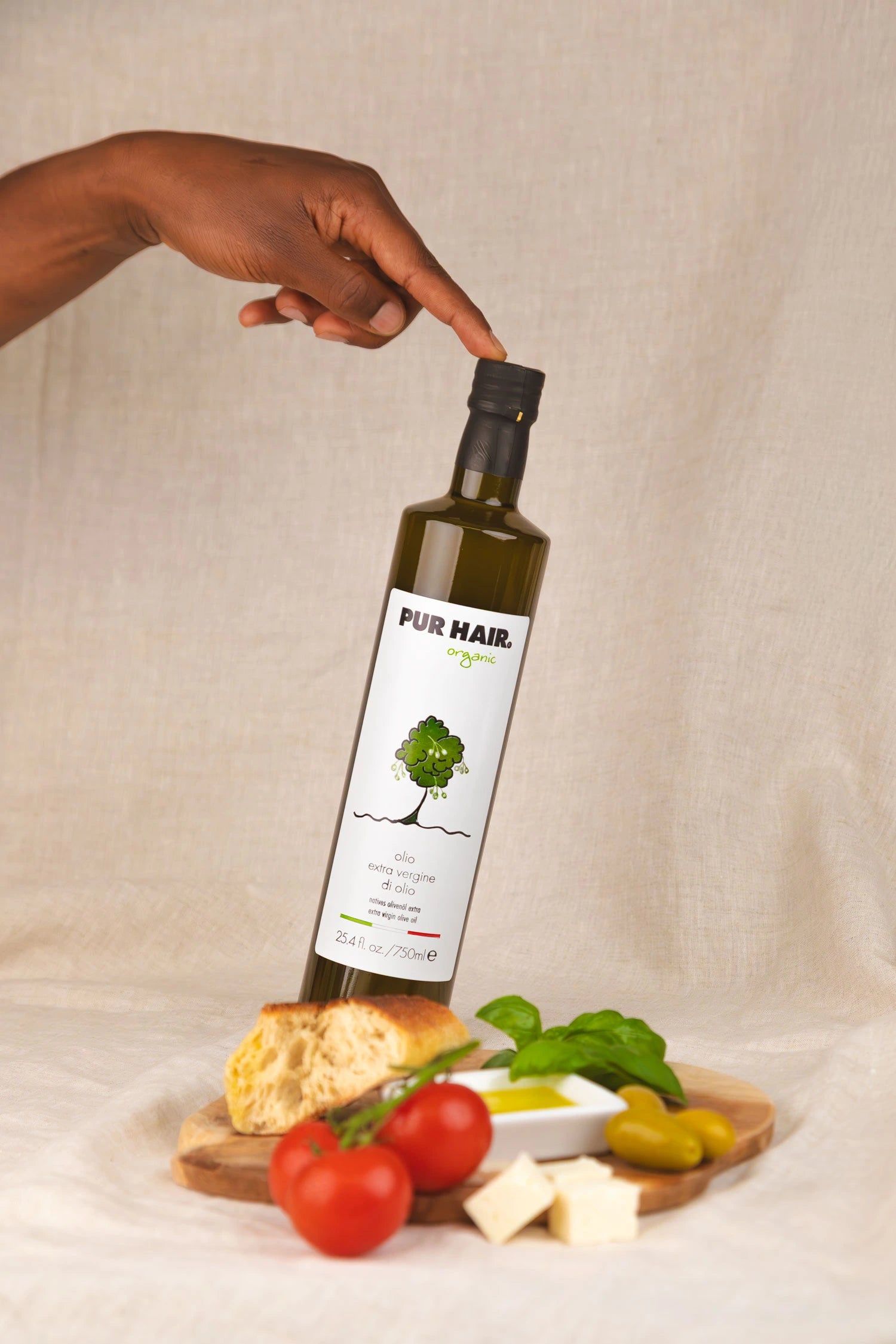 Flasche natives Bio-Olivenöl extra, 750 ml, mit Etikett und Olivenbaum-Illustration, im Vordergrund Brot, Tomate und Basilikum