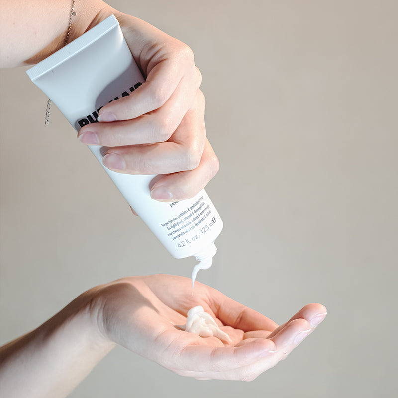 Hand drückt weiße Haarpflegecreme aus PUR HAIR Organic Tube
