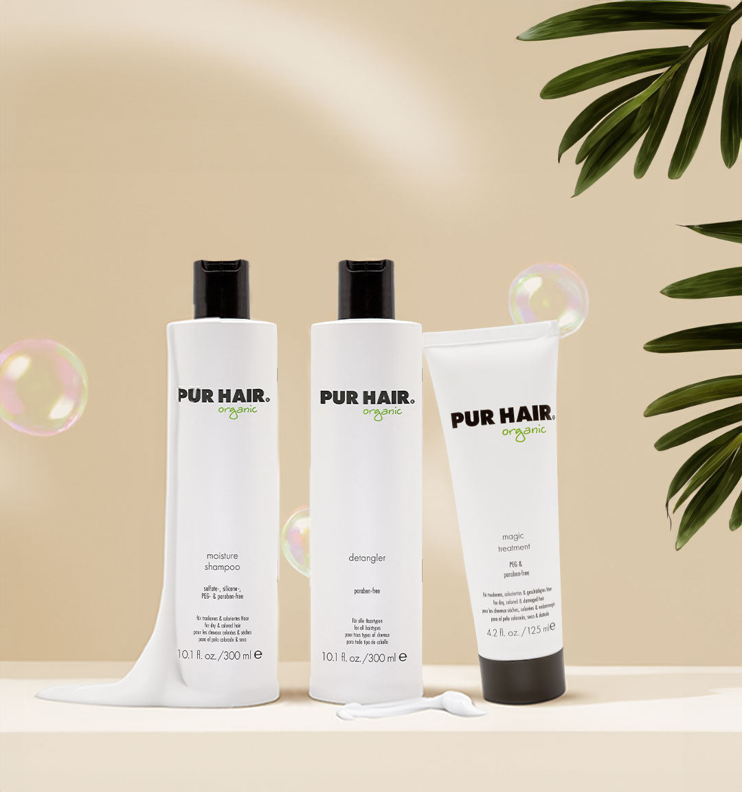 Drei PUR HAIR Organic Produkte – Moisture Shampoo, Detangler und Magic Treatment – auf hellem Hintergrund mit grünen Blättern und Seifenblasen dekoriert