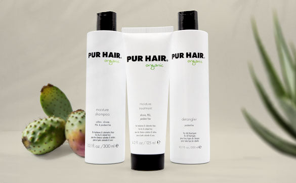 Drei PUR HAIR Organic Produkte – Moisture Shampoo, Moisture Treatment und Detangler – vor Naturdeko mit Kaktusfeige und grünem Blatt
