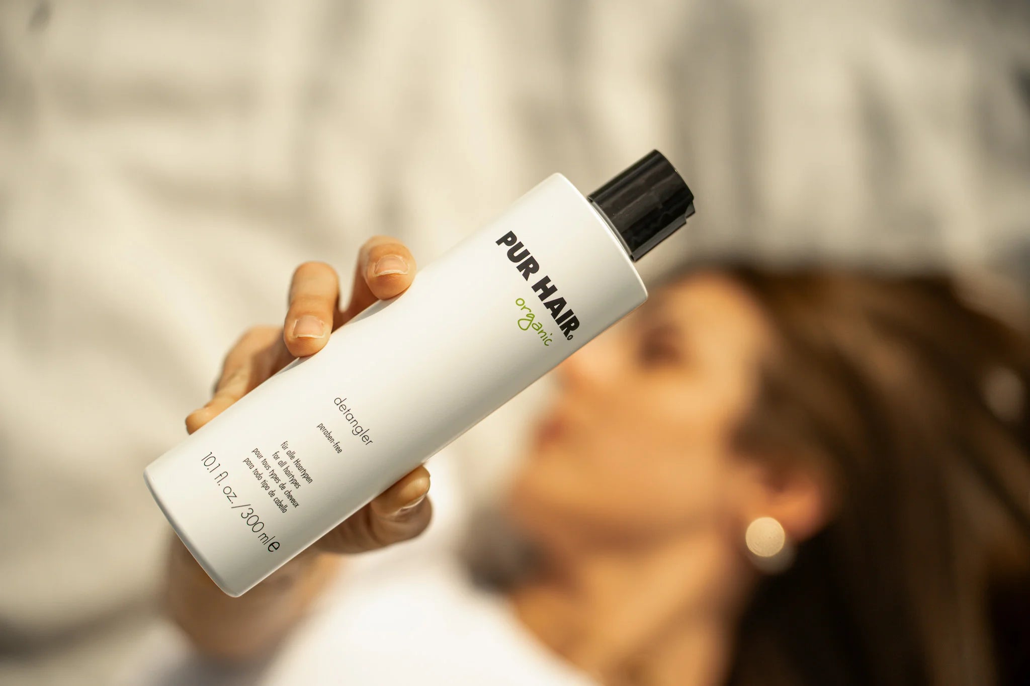 PUR HAIR Detangler in 300 ml, Frau hält die Flasche und ist verschwommen
