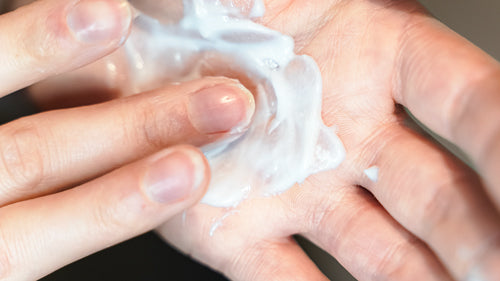 Nahaufnahme von Händen, die eine weiße Haarpflege-Creme in den Handflächen verreiben