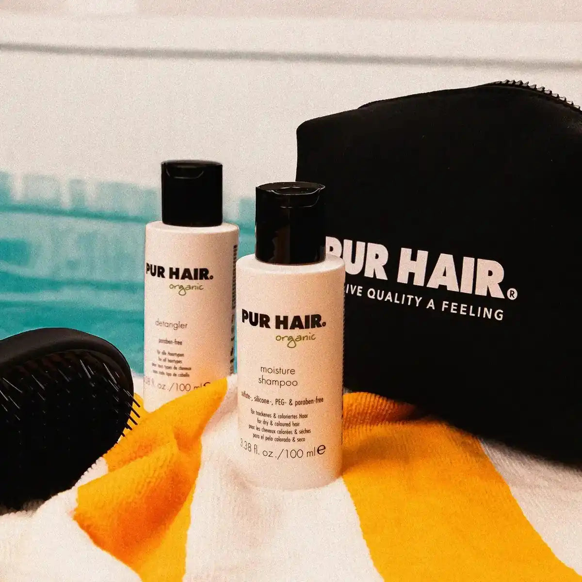 PUR HAIR Moisture Travel Set, weiße Flaschen, stehen vor dem Pool, auf orange-weiß gestreiftem Handtuch