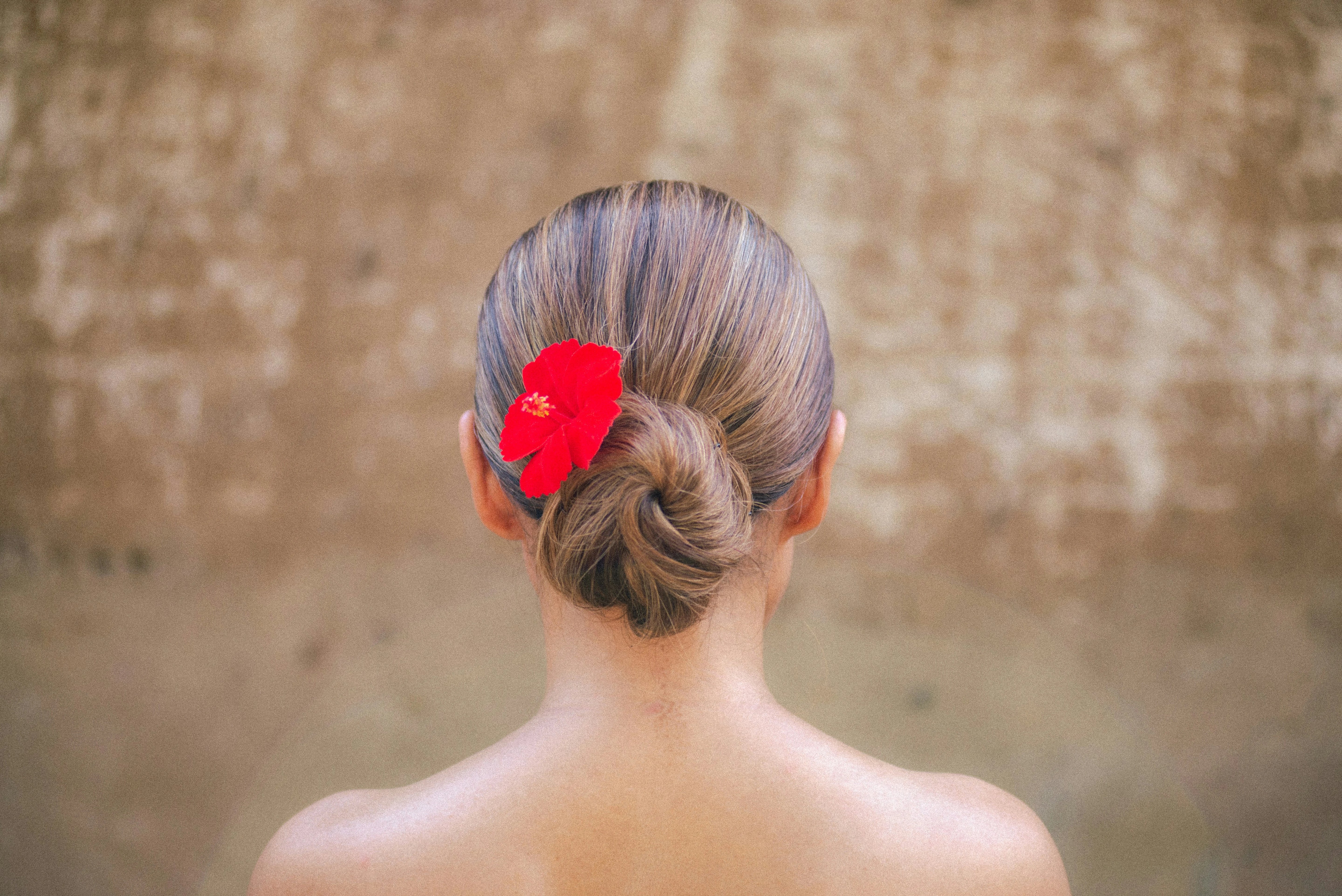 Frau mit blondem Dutt im Nackenbereich, mit roter Hibiskusblüte im Haar