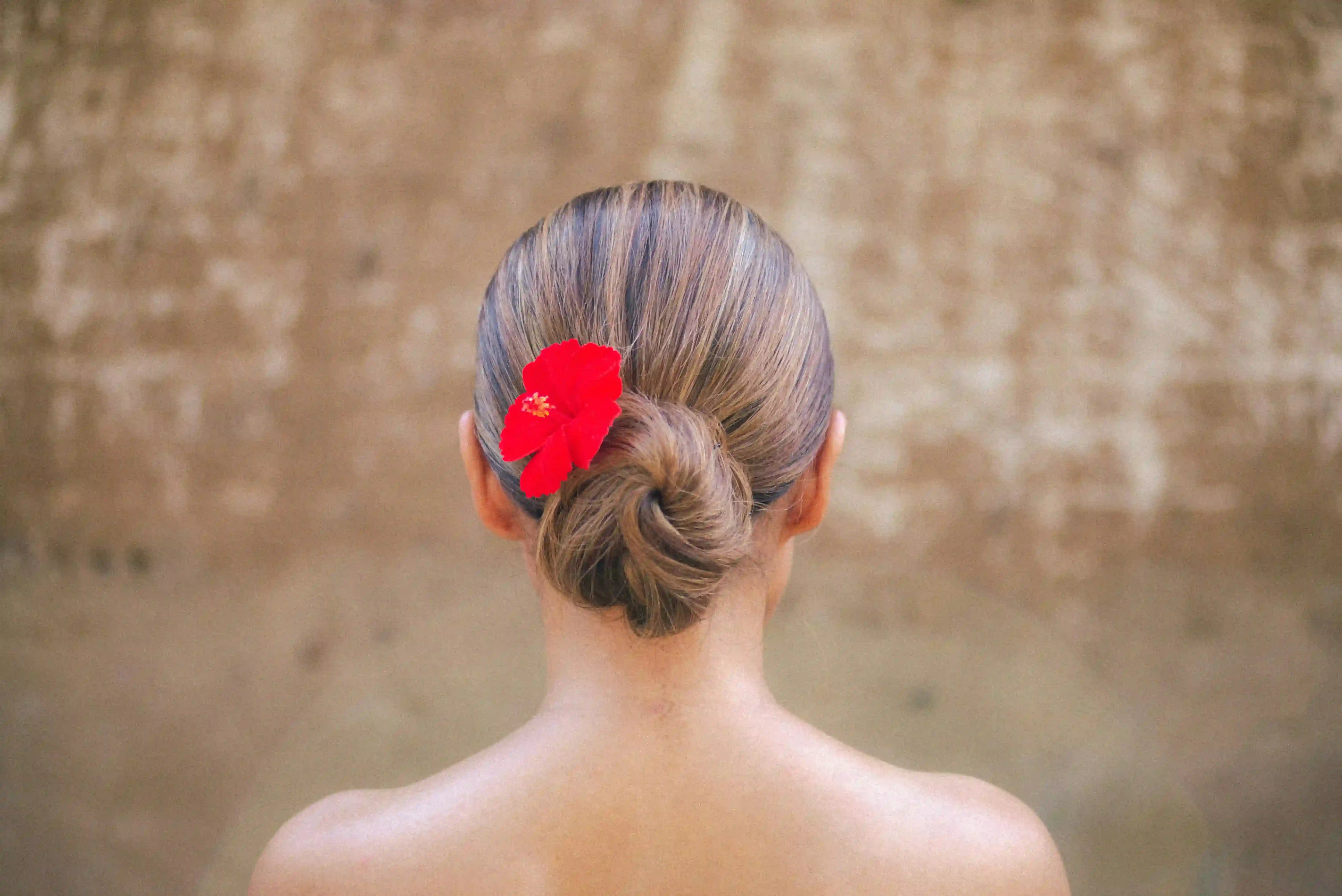 Frau mit blondem Dutt im Nackenbereich, mit roter Hibiskusblüte im Haar