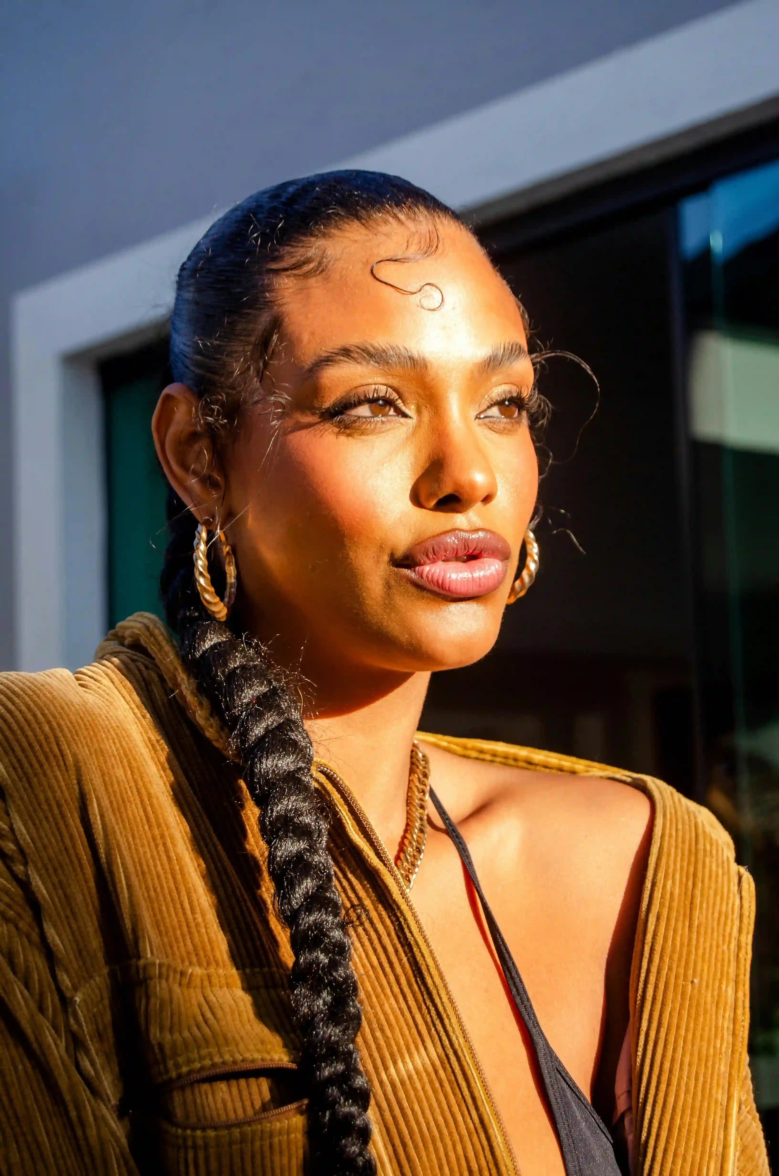 Frau mit langen dunklem Zopf, goldenen Ohrringen, orangener Jacke, wird von der Sonne angestrahlt