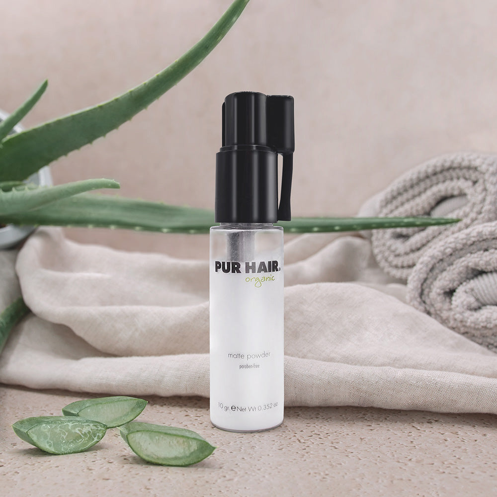 PUR HAIR Organic Matte Powder in transparenter Flasche mit Pumpspender, stilvoll inszeniert neben Aloe-Vera-Blättern und Handtüchern – mattierendes Volumenpuder für griffiges Haar ohne Parabene