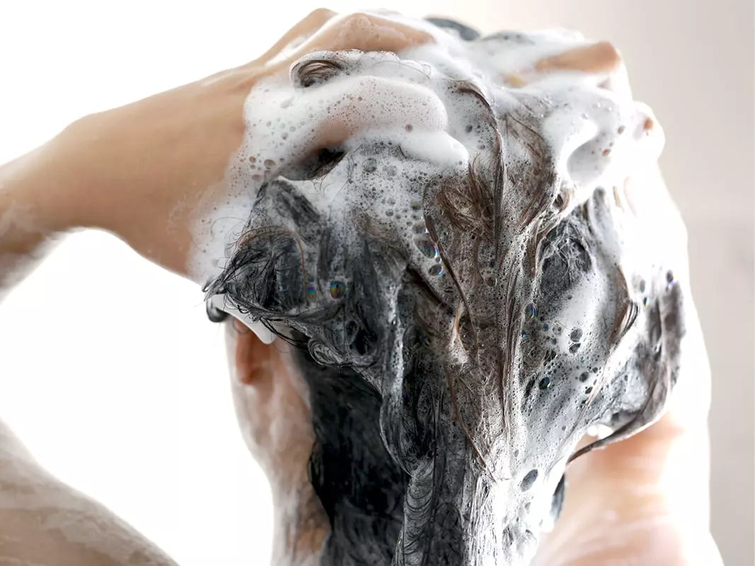 Frau von hinten schäumt sich die Haare mit Shampoo