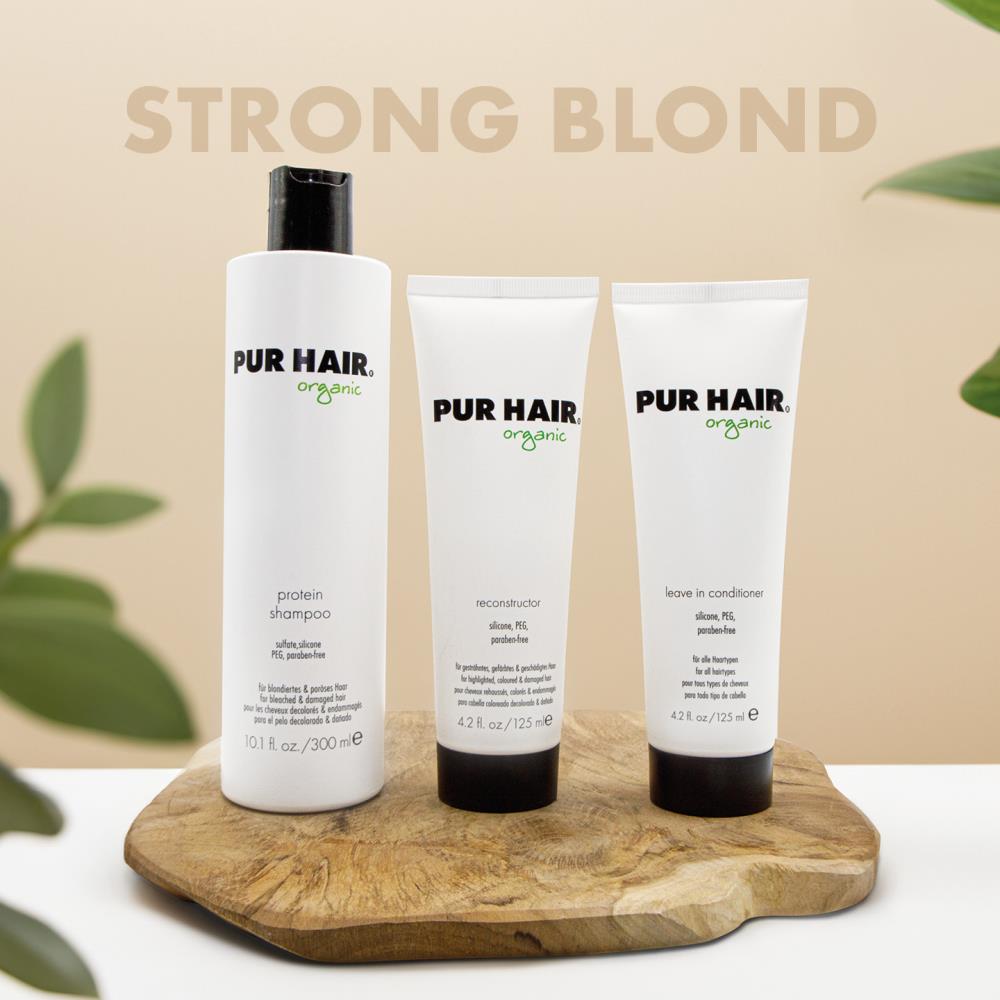 PUR HAIR Organic Blond Set bestehend aus Protein Shampoo, Reconstructor und Leave In Conditioner. Die drei weißen Flaschen und Tuben stehen dekorativ auf einem Holzbrett vor einem pastell-braunen Hintergrund mit der Aufschrift ‚Strong Blond‘