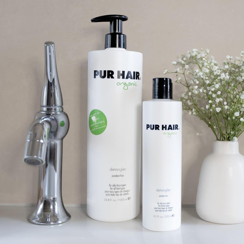 PUR HAIR Detangler in 300 ml und 1000 ml Flasche stehen neben Blumenwase und silbernen Wasserhahn