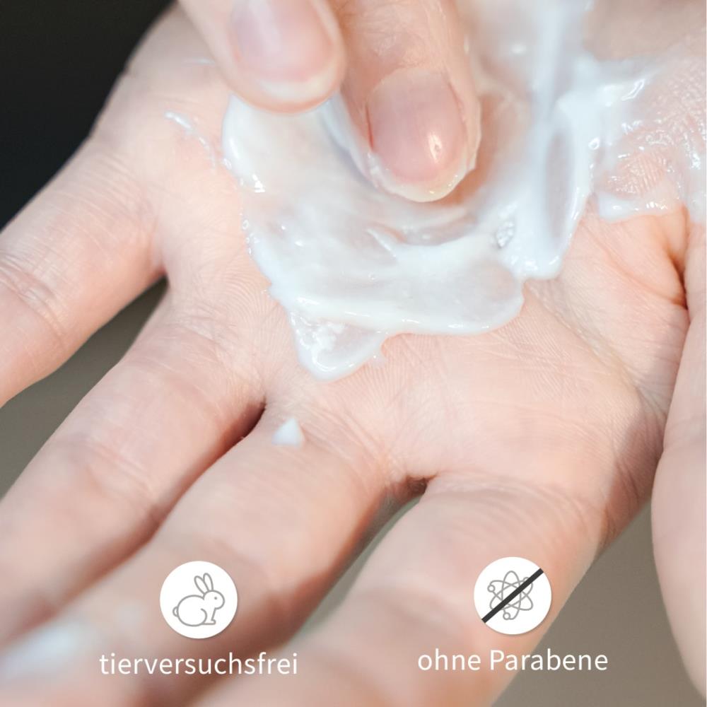 Hand verteilt weiße Haarpflege-Creme, Symbole im Bild: tierversuchsfrei und ohne Parabene