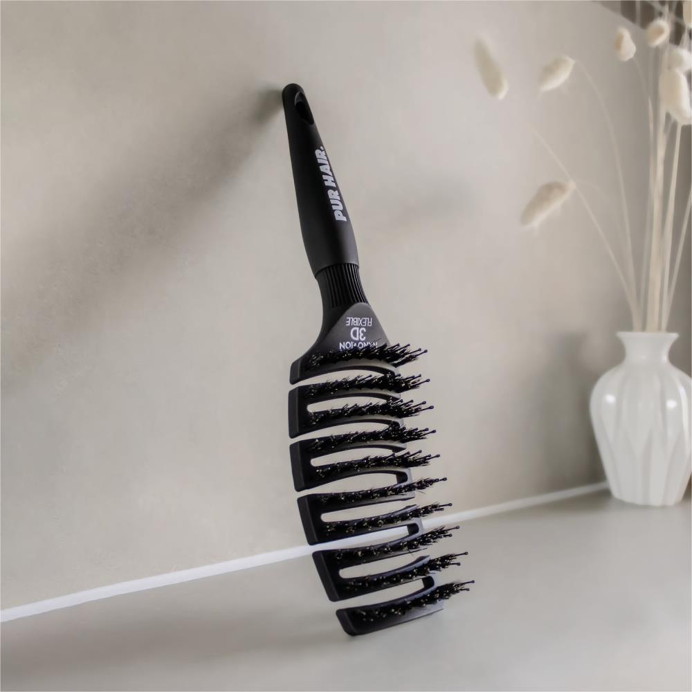 Schwarze PUR HAIR Magic Flex Brush mit 3D-Flexibilität lehnt an einer grauen Wand, moderne Szene mit dekorativer Vase im Hintergrund