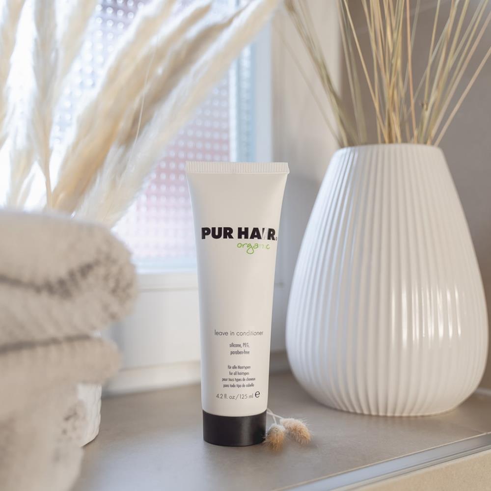 PUR HAIR Organic Leave-in Conditioner, 125 ml Tube mit schwarzem Deckel, dekorativ im Badezimmer neben Handtüchern und Vase aufgestellt