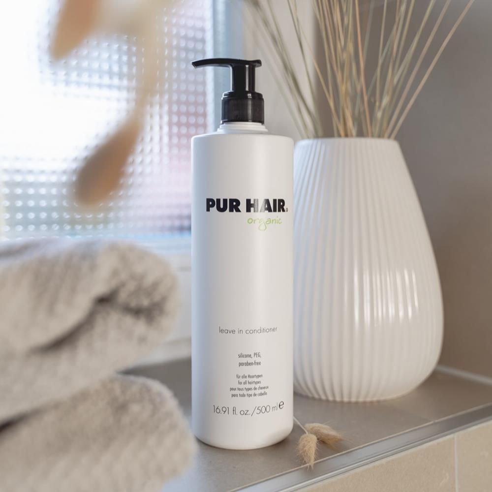 PUR HAIR Organic Leave-in Conditioner, 500 ml Flasche mit Pumpspender, dekorativ im Badezimmer neben Handtüchern und Vase aufgestellt