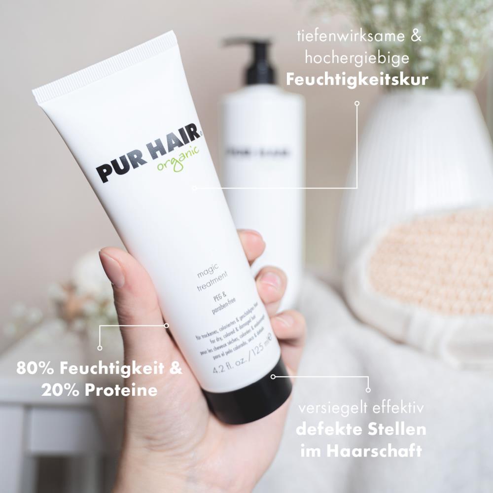PUR HAIR Organic Magic Treatment in 125 ml Tube wird in der Hand gehalten, im Hintergrund weiße Blüten und eine große Flasche; Text weist auf Feuchtigkeitspflege, 80 % Feuchtigkeit, 20 % Proteine, versiegelt effektiv defekte Stellen am Haar