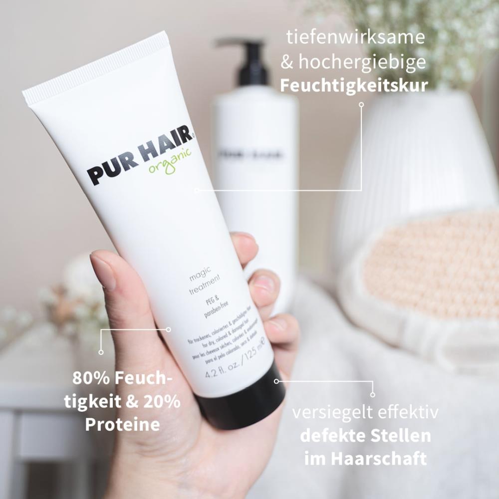 PUR HAIR Organic Magic Treatment in 125 ml Tube wird in der Hand gehalten, im Hintergrund weiße Blüten und eine große Flasche; Text weist auf Feuchtigkeitspflege, 80 % Feuchtigkeit, 20 % Proteine, versiegelt effektiv defekte Stellen am Haar