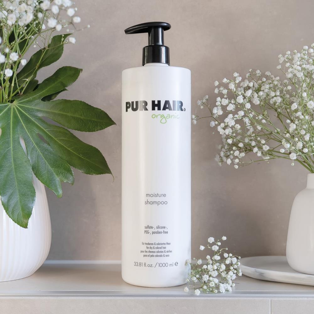 PUR HAIR Organic Moisture Shampoo, 1000 ml Flasche in Weiß mit schwarzem Pumpspender, dekorativ neben Vase mit Blumen