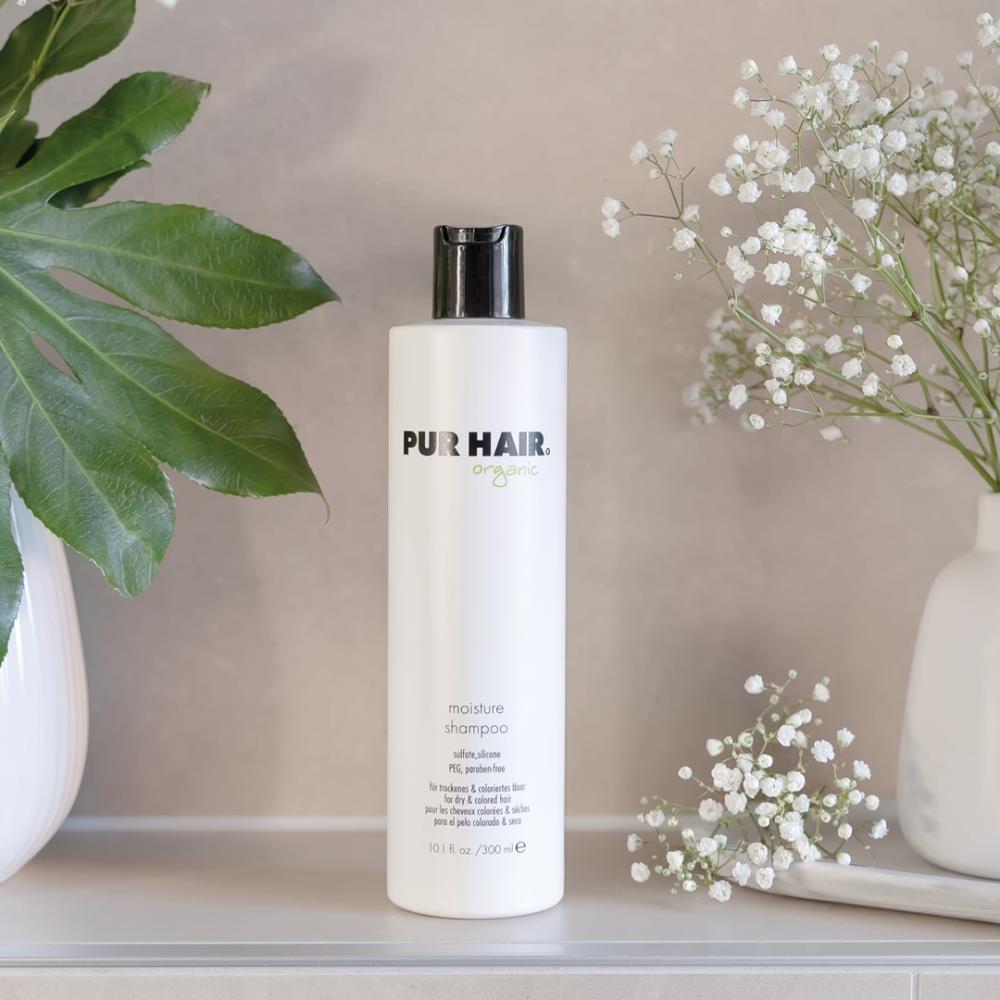 PUR HAIR Organic Moisture Shampoo, 300 ml Flasche in Weiß mit schwarzem Deckel, neben Vase mit Blumen