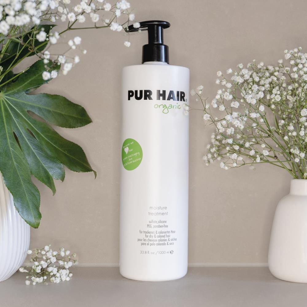 PUR HAIR Organic Moisture Treatment, 1000 ml Flasche in Weiß mit schwarzem Pumpspender, dekorativ neben Vase mit Blumen