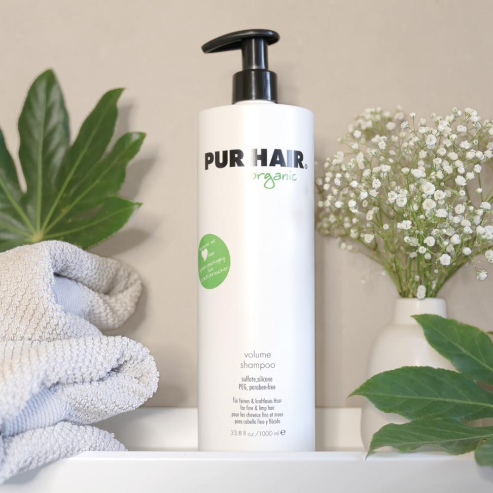Weiße 1000 ml Flasche PUR HAIR Organic Volume Shampoo mit Pumpspender, dekoriert mit Handtuch, Grünpflanzen und Vase mit weißen Blüten