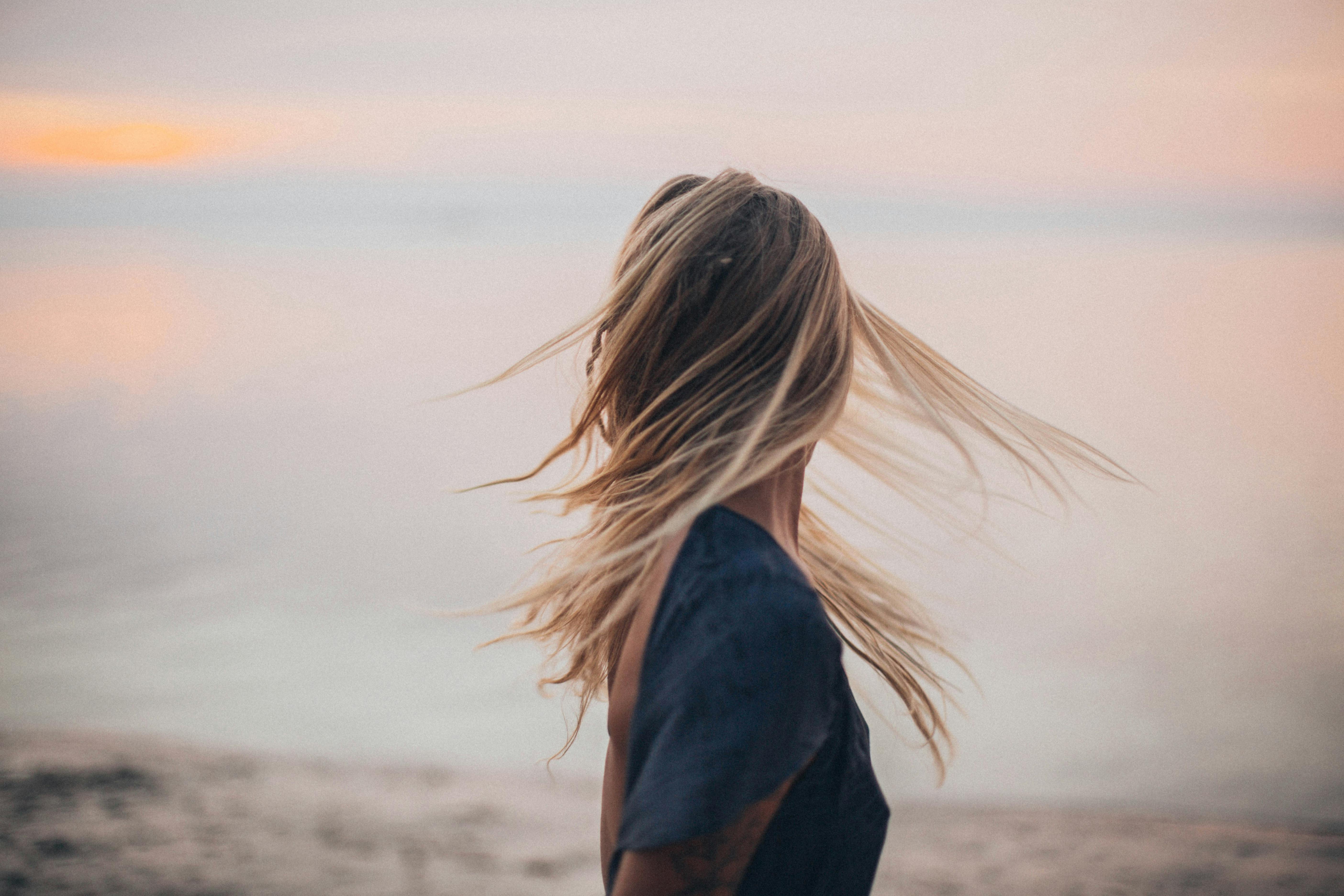 Person mit langen Haaren, die sich bei Sonnenuntergang am Strand dreht, während ihr Haar im Wind weht.