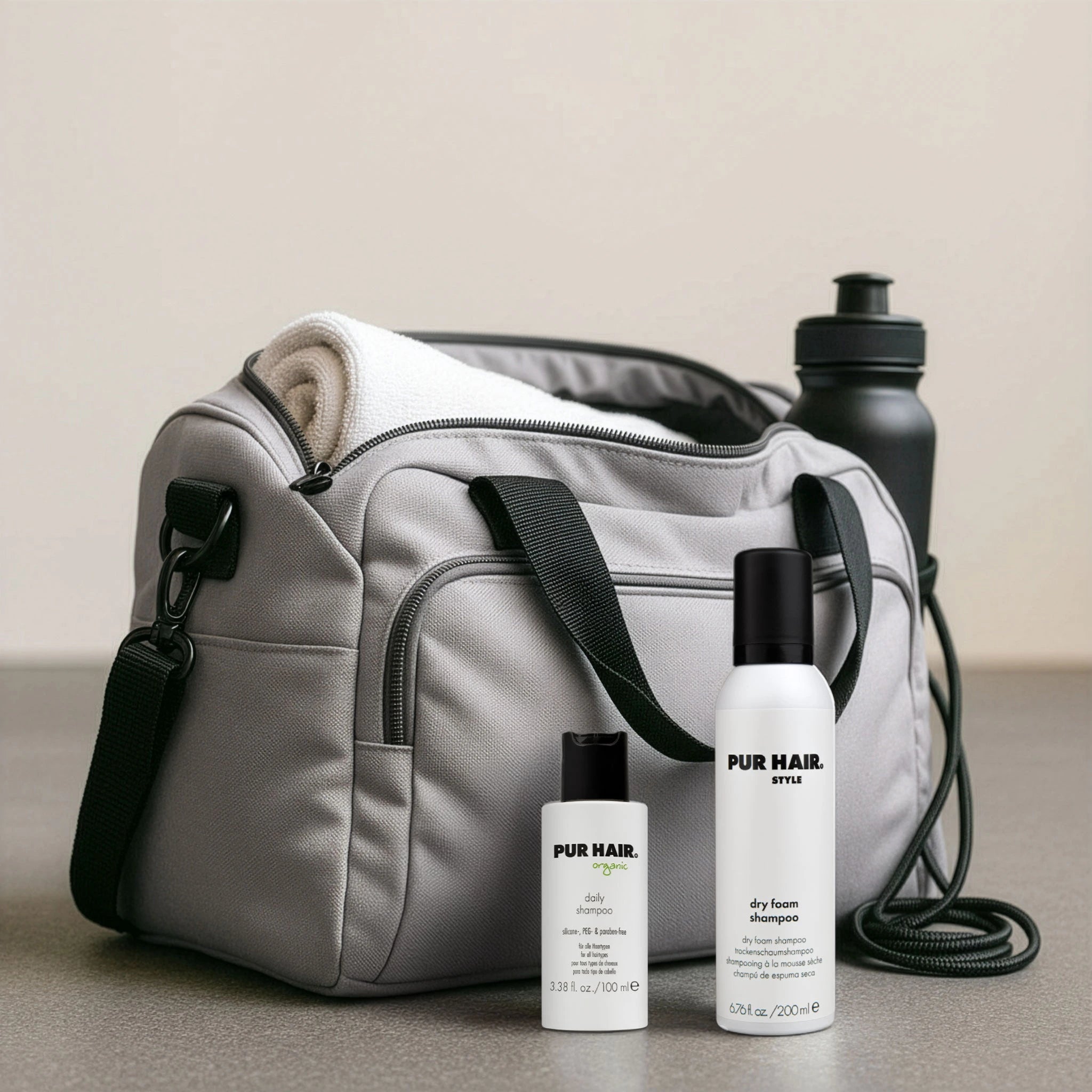 Graue Sporttasche mit weißen Flaschen vom Daily Shampoo 100 ml und Dry Foam Shampoo.
