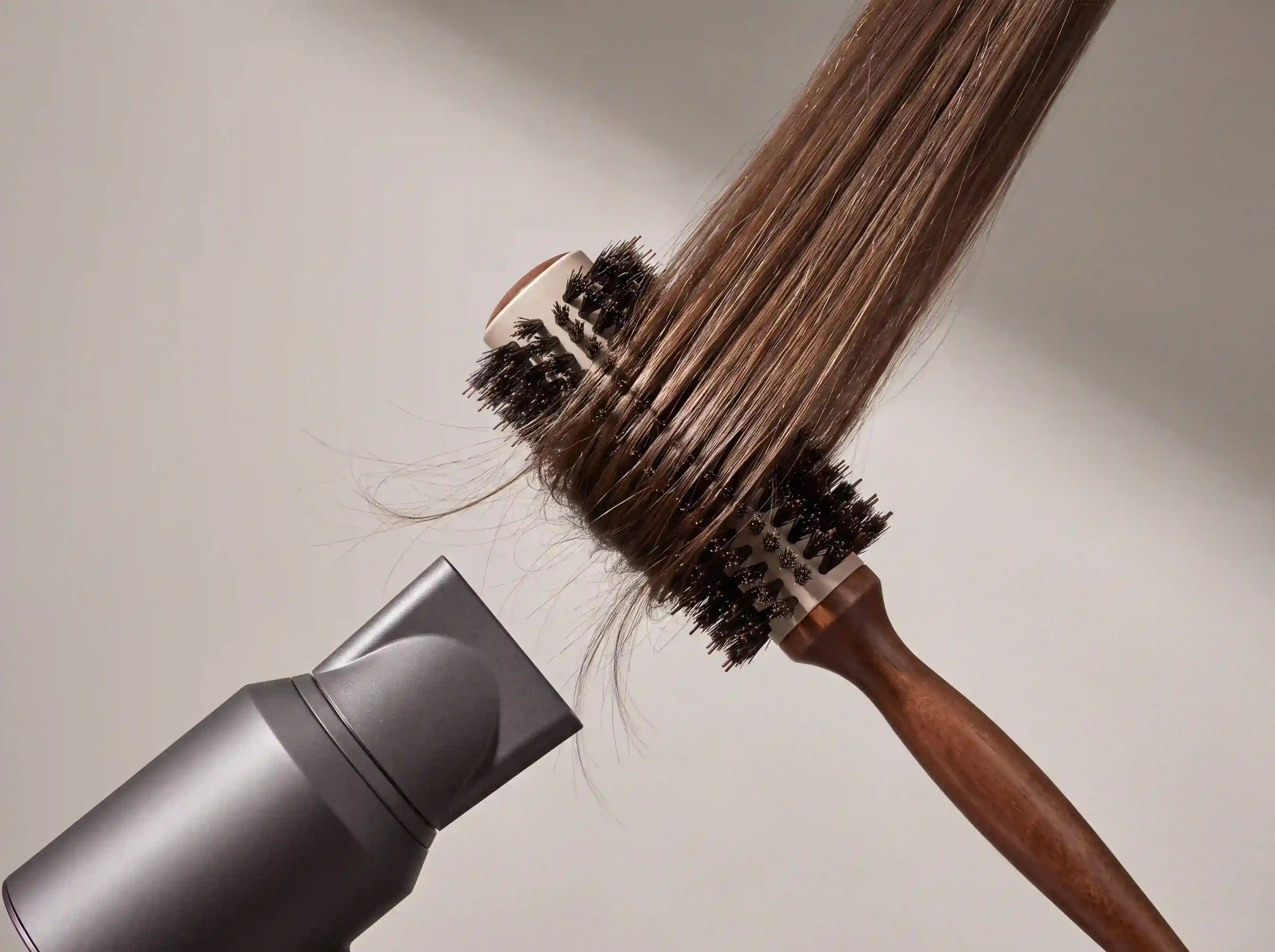 Braune Haarsträhne wird mit Rundbürste und Föhn gestylt, um Volumen und Form in das Haar zu bringen.
