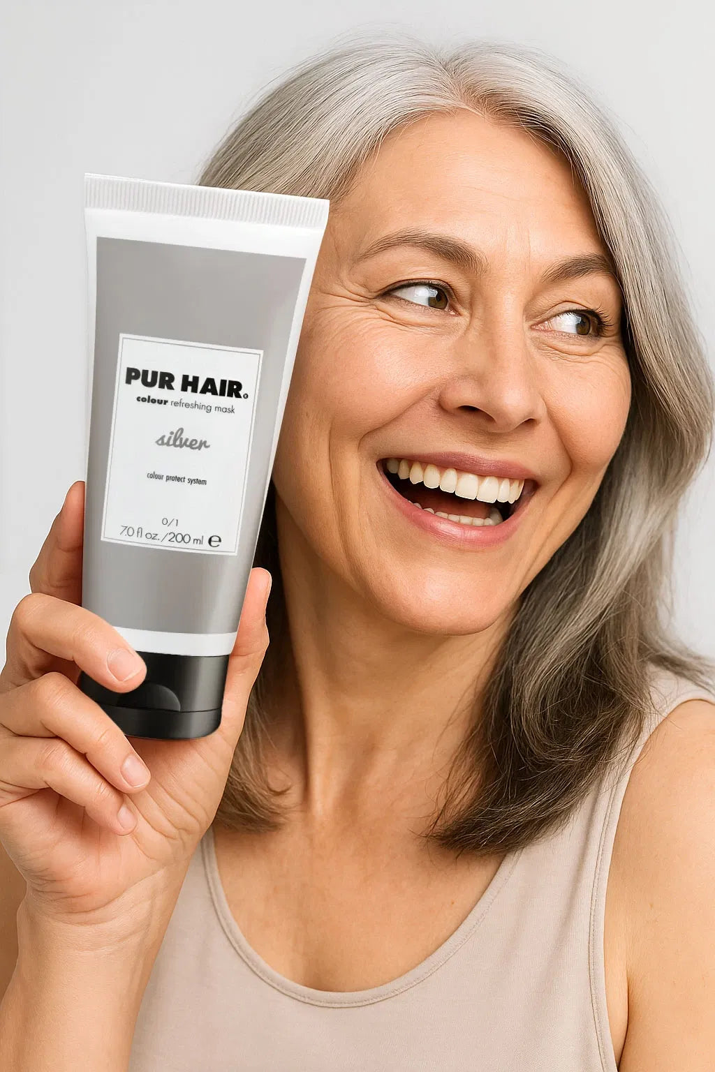 Eine Frau mit grauem Haar lächelt zur Seite und hält die PUR HAIR Colour Refreshing Mask silver in der Hand.