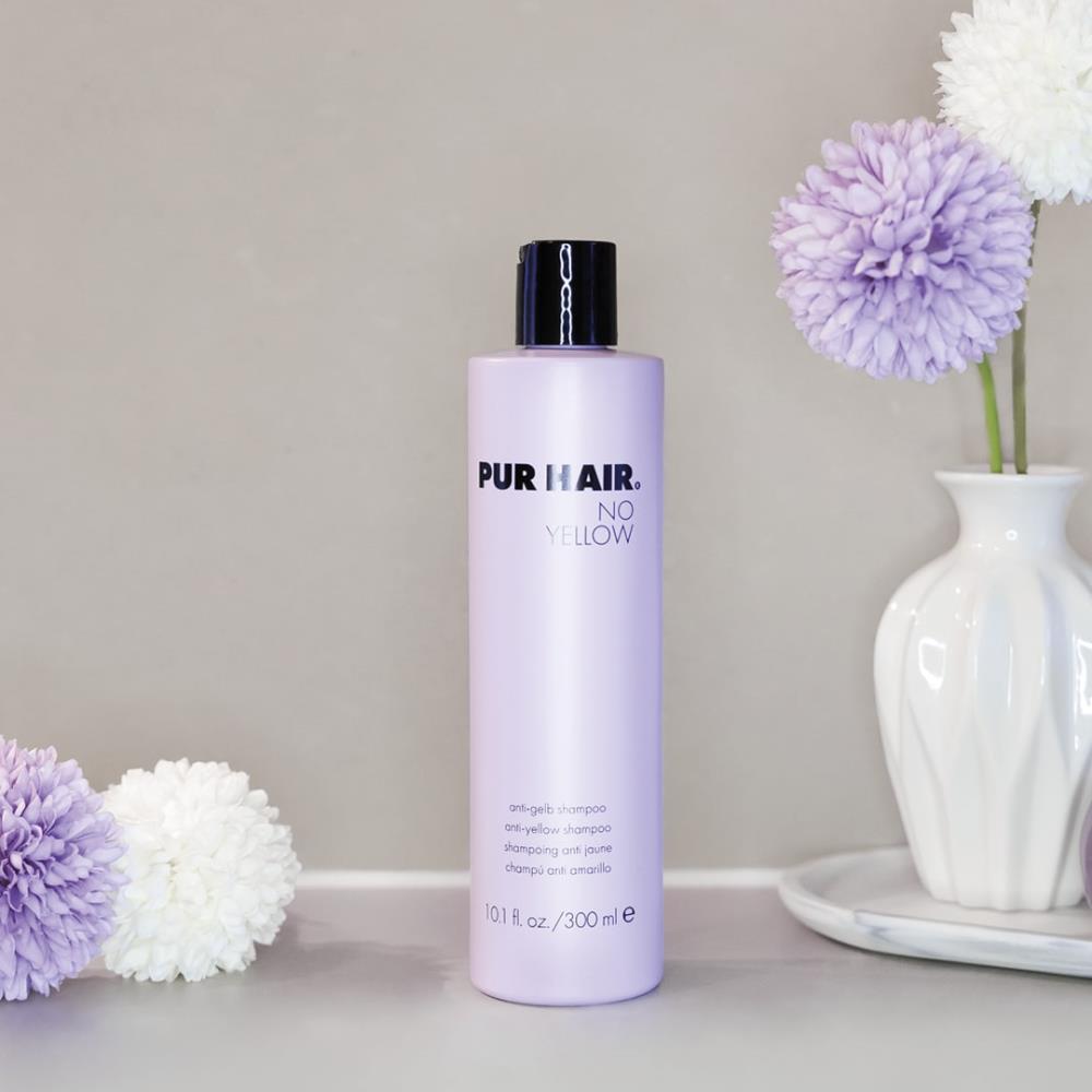 Weiße Flasche PUR HAIR No Yellow Shampoo, 300 ml, neben violetten Trockenblumen im Badezimmer platziert